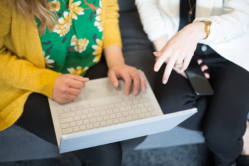 Two colleagues working side by side at a laptop keyboard